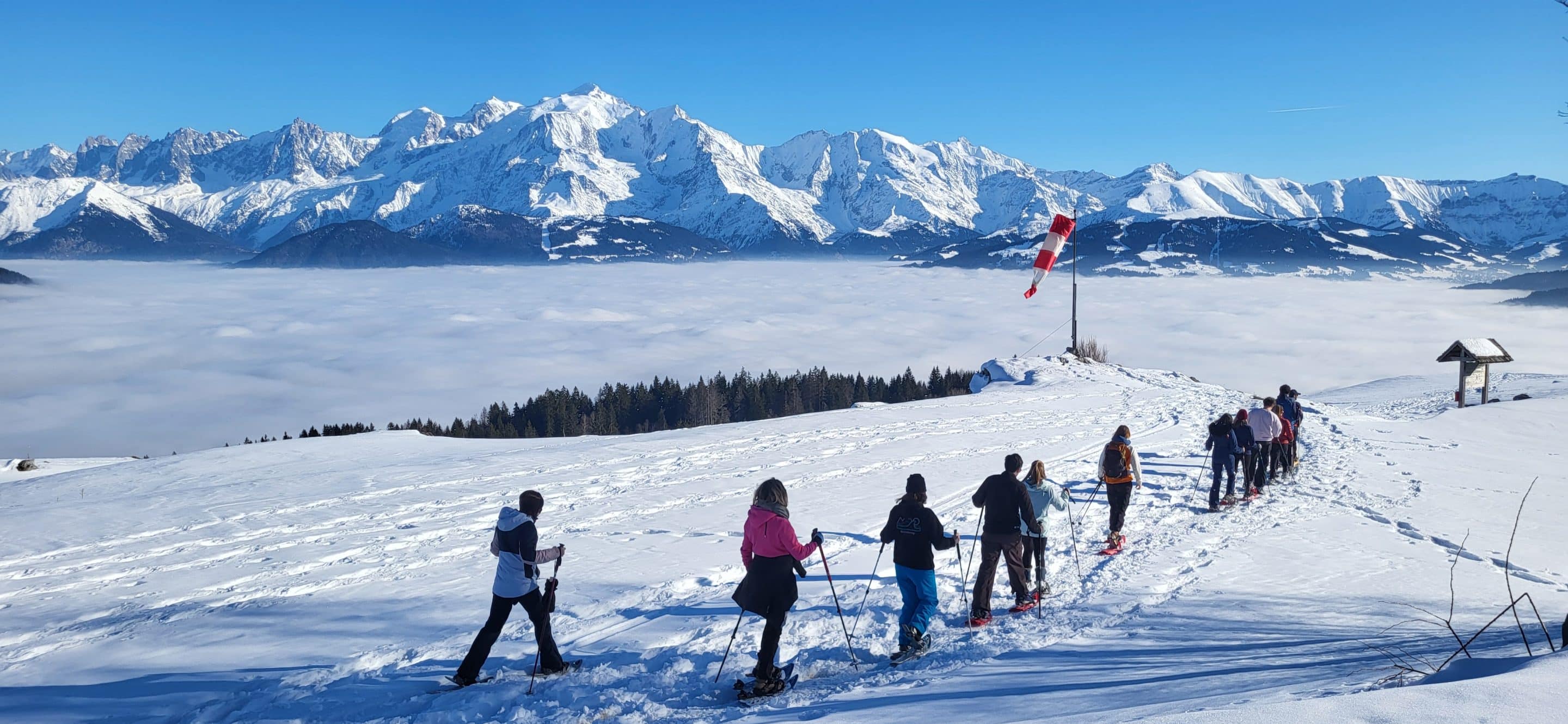 Corporate group snowshoeing above a sea of clouds, facing the Mont-Blanc massif